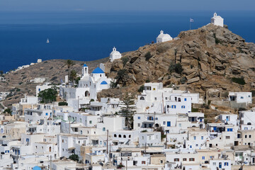 Panoramic view of a church, smaller chapels and the Greek flag on the top of a hill overlooking the Aegean Sea in  Ios in Greece, also known as Chora