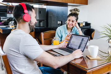 young latin couple working on laptop with headphones at home in Mexico, hispanic people home office	