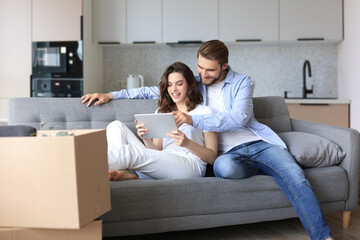 Happy couple sitting and planning new home decoration at home with a tablet at moving day,...
