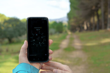 woman orienting herself in the forest with her smart phone's compass following a trail in the pine...