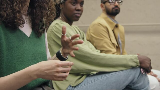 Close-up shot of hands of unrecognizable young woman sitting among diverse audience at corporate training, asking question to speaker, and gesticulating