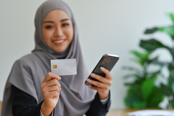 Beautiful Muslim woman in hijab holding mobile phone and credit card, enjoy shopping on internet.