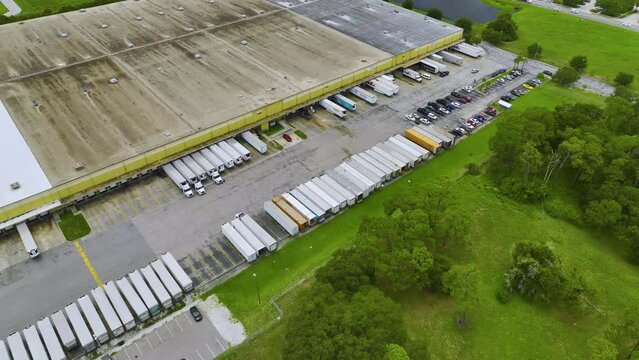 Large commercial distribution storehouse with many semitrucks unloading and uploading retail products for international shipment. Global market economy concept