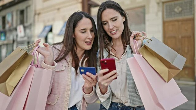 Two women going shopping using smartphone and credit card at street