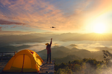 A woman use drone for take a photo landscape between sunrise  and fog background at top of mountain at Tak
