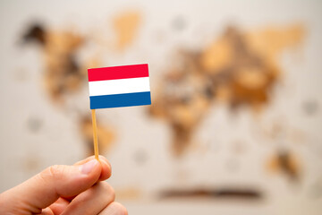 Netherlands flag in mans hand on the wooden world map background. Global economy and geopolitics...