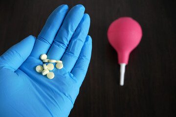 hand holding  pills on enema  on wooden background, enema vs pills for treatment  from intestinal constipation