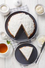 Boston bun, also known as a Sally Lunn, is a large spiced bun with a thick layer of coconut icing closeup on the table. Vertical top view from above