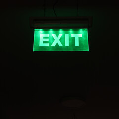 Green exit sign letters symbol glowing in the dark emergency escape way. Escape from darkness in the light concept idea