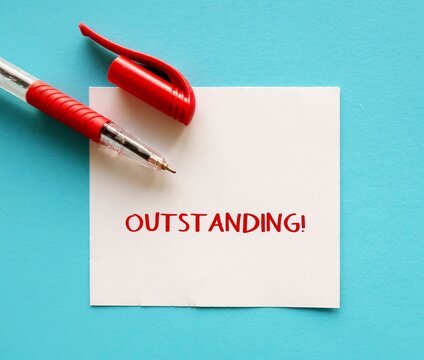 Red pen writing on note on blue background with handwritten OUTSTANDING!, compliment praise giving to someone to tell they are doing great work or awesome job, Boss admire worker for impressive job