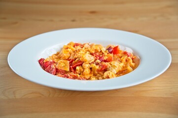 Close up of a typical hungarian homemade lecso (in hungarian: lecsó) from tomatoes, peppers, onions and eggs on white plate, wooden table. 