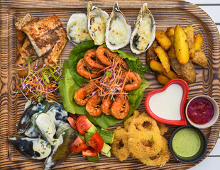 A lot of seafood as fried fish, calamari, oysters and sauces on wooden board on the table