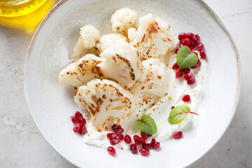 Beige plate with roasted cauliflower florets, cream-cheese and pomegranate seeds, horizontal shot, middle close-up