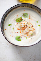 Close-up of cream-soup made from cauliflower cabbage, vertical shot on a light-beige stone background, elevated view