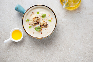 Turquoise serving bowl with cauliflower cream-soup, top view on a beige stone background, horizontal shot with copy space