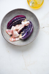 Grey plate with bbq red cabbage and bacon, high angle view on a light-beige marble background, vertical shot, copy space