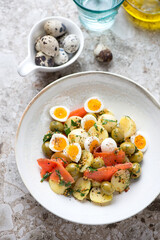 Salad with baby potato, red fish, quail eggs and olives, vertical shot on a light-brown granite background, elevated view