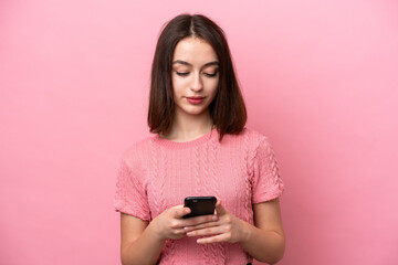 Young Ukrainian woman isolated on pink background using mobile phone