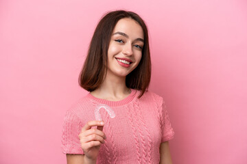 Young Ukrainian woman holding invisible braces isolated on pink background smiling a lot