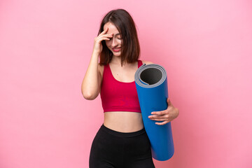 Young sport Ukrainian woman going to yoga classes while holding a mat isolated on pink background laughing