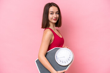 Young Ukrainian woman isolated on pink background with weighing machine