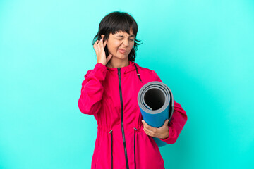 Obraz premium Young girl going to yoga classes while holding a mat isolated on blue background frustrated and covering ears