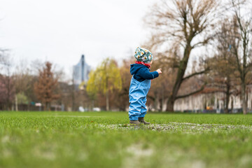 A little child playing in a puddle in a park during rainy weather