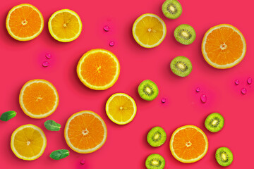 Fresh juicy slices of orange, kiwi fruit and lemon on bright red background covered with water drops. Creative food background, top view