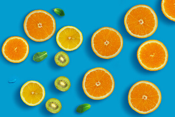 Fresh juicy slices of orange, kiwi fruit, lemon and mint leaves on bright blue background. Creative food background, top view