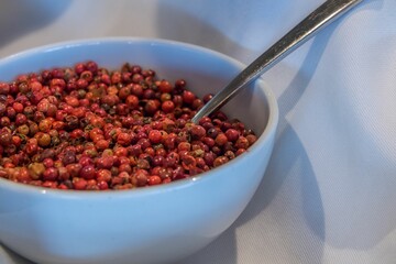 Closeup shot of a white bowl filled with dried pink peppercorn