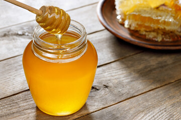 honey in jar with dipper and honeycomb on wooden table
