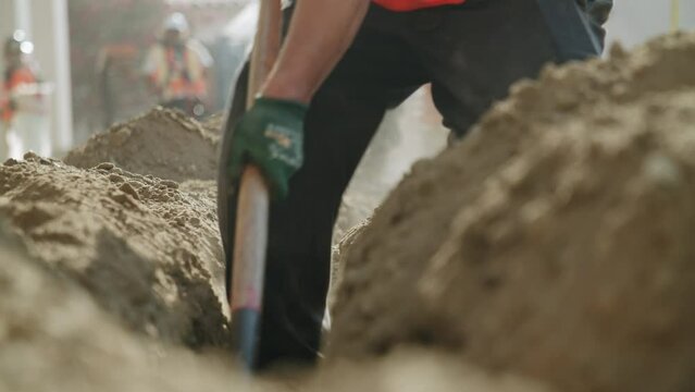 Closeup of the construction sand and soil and a builder digging it with a special shovel