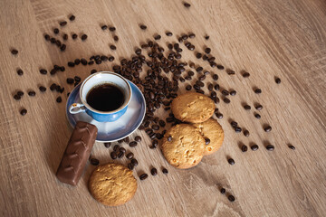 Roasted coffee beans and cup of coffee with drink on dark wooden surface, nearby lies chocolate and...