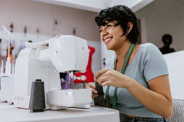 Young latin woman fashion designer working with a sewing machine at her workshop in Mexico Latin...