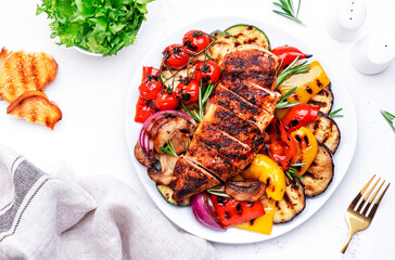 Grilled vegetables and chicken breast fillet. Colorful paprika, zucchini, eggplant, mushrooms, tomatoes, onion and rosemary, served on plate, white table background, top view