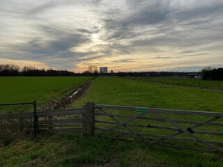 Fototapeta premium Fields with wooden fence and dramatic sunset cloudy sky on the horizon