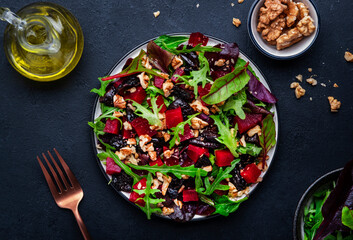 Healthy salad with beet, prunes, arugula, chard and walnuts, black table background. Fresh useful vegan dish for healthy eating