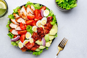 Cobb salad with chicken fillet, tomatoes, eggs, bacon, avocado and lettuce, gray table background, top view. American cuisine dish