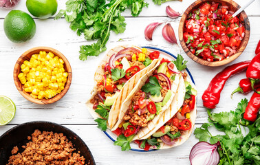 Tacos with beef, corn, red beans, tomato salsa sauce and red onions in corn tortilla on plate. Mexican cuisine. White table background, top view