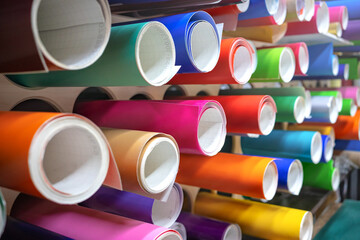 Rolls of multicolored vinyl film on the shelves. Self-adhesive film for pasting shop windows and vehicles.External tuning of the car. Workshop for the production of outdoor advertising