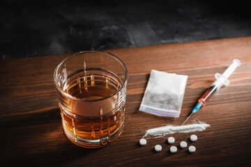 Alcohol drink in a glass, syringe with a dose of drugs, white pills and narcotics powder in a...