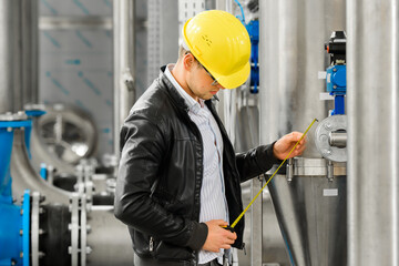 A young engineer is measuring with a tape measure at the factory.