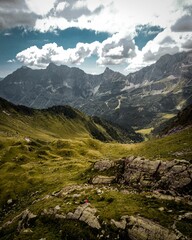 Vertical aerial view of a person on a rock in a green mountain range under a cloudy blue sky