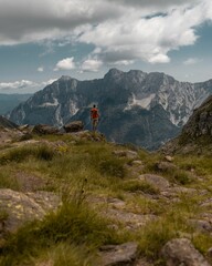 Vertical shot of a person hiking in green mountains under a cloudy blue sky