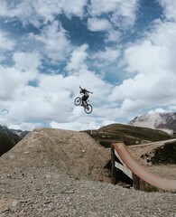 Vertical shot of a person doing tricks with their bike above a rocky hill