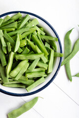 Fresh green beans in a bowl on a white wooden table. Bowl of green beans on wooden background. Top view.