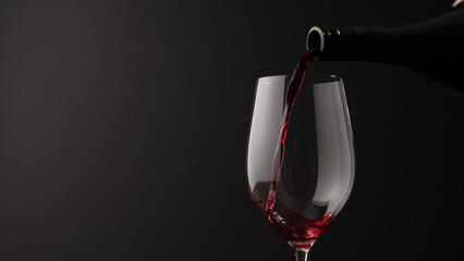 Naklejka na ściany i meble pour red wine into wineglass on black background