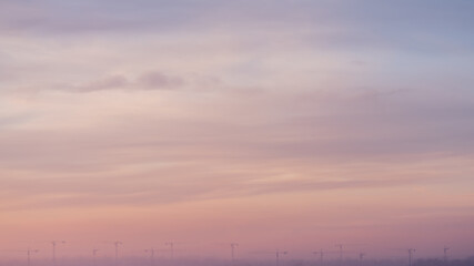 Dramatic sunset sky with clouds and construction cranes far away