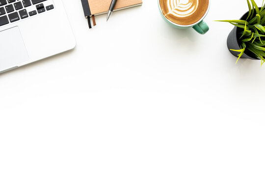 White office desk table with laptop computer, cup of hot latte coffee and office supplies. Top view with copy space, flat lay.