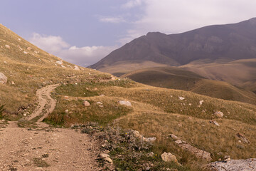 Mountains landscape - country road in mountain valley with hilly slopes and ridges in sunny autumn day with and golden sunbeams, yellow dried meadow. Joyful travel in Dagestan.